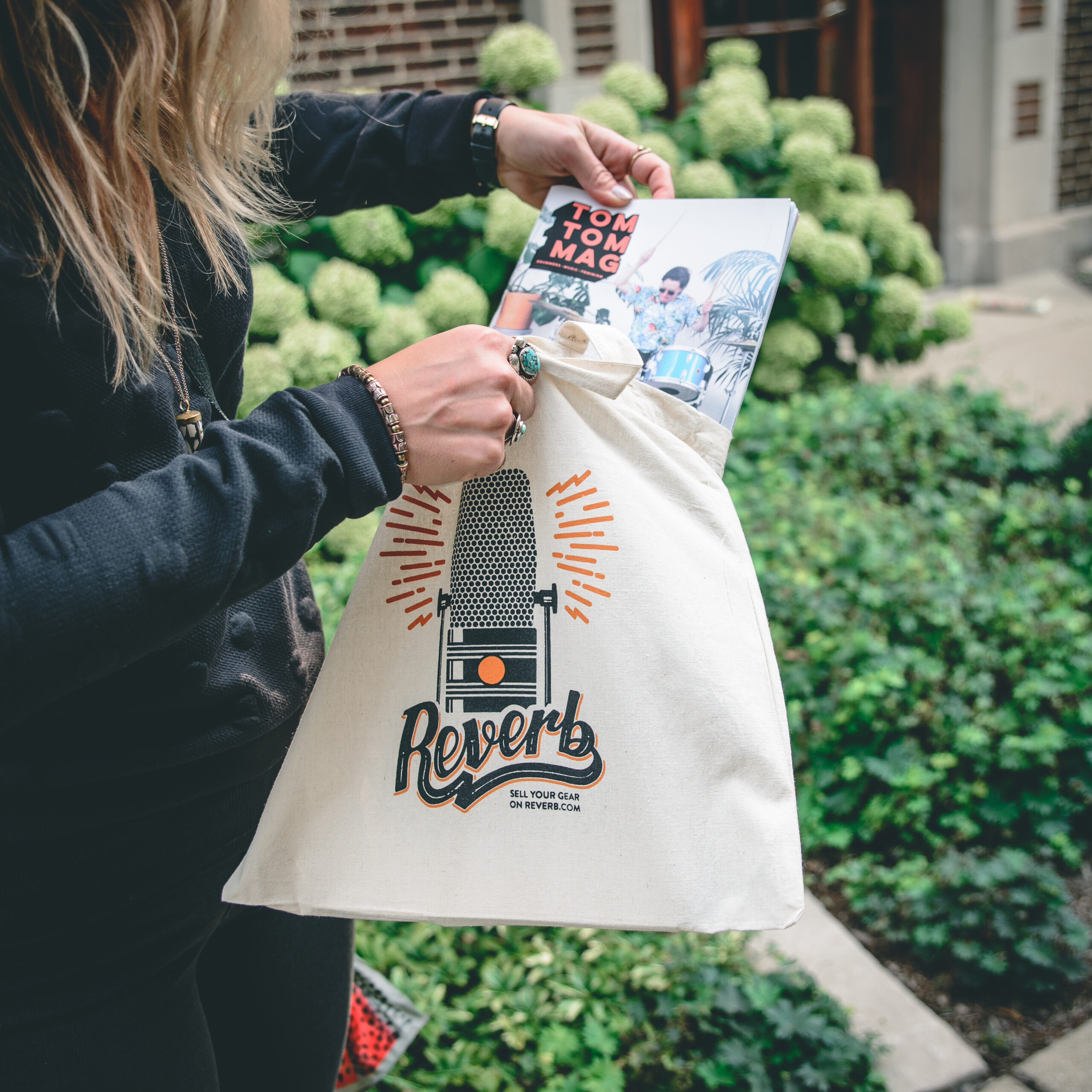 A person putting a magazine into a tote bag with a microphone illustration on it