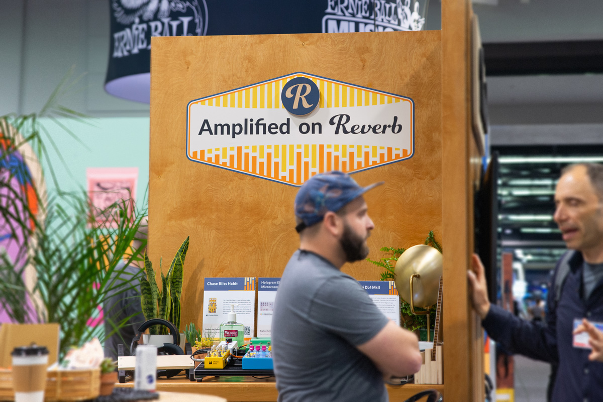 Wide shot of the gear kiosk with signage, with a view of the surrounding NAMM floor